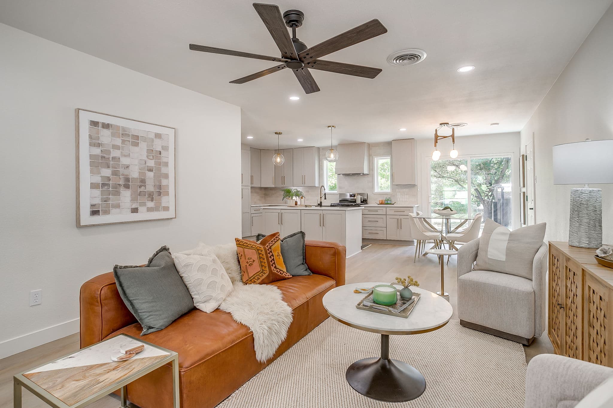 Modern open-concept living room featuring a brown leather sofa, marble coffee table, and kitchen.