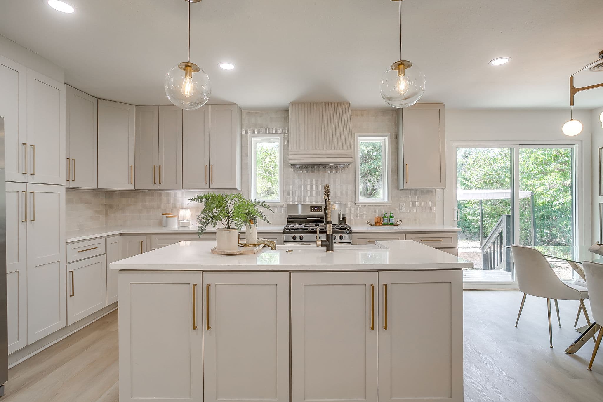 Modern kitchen with light gray cabinets, gold hardware, a large island, and globe pendant lights.
