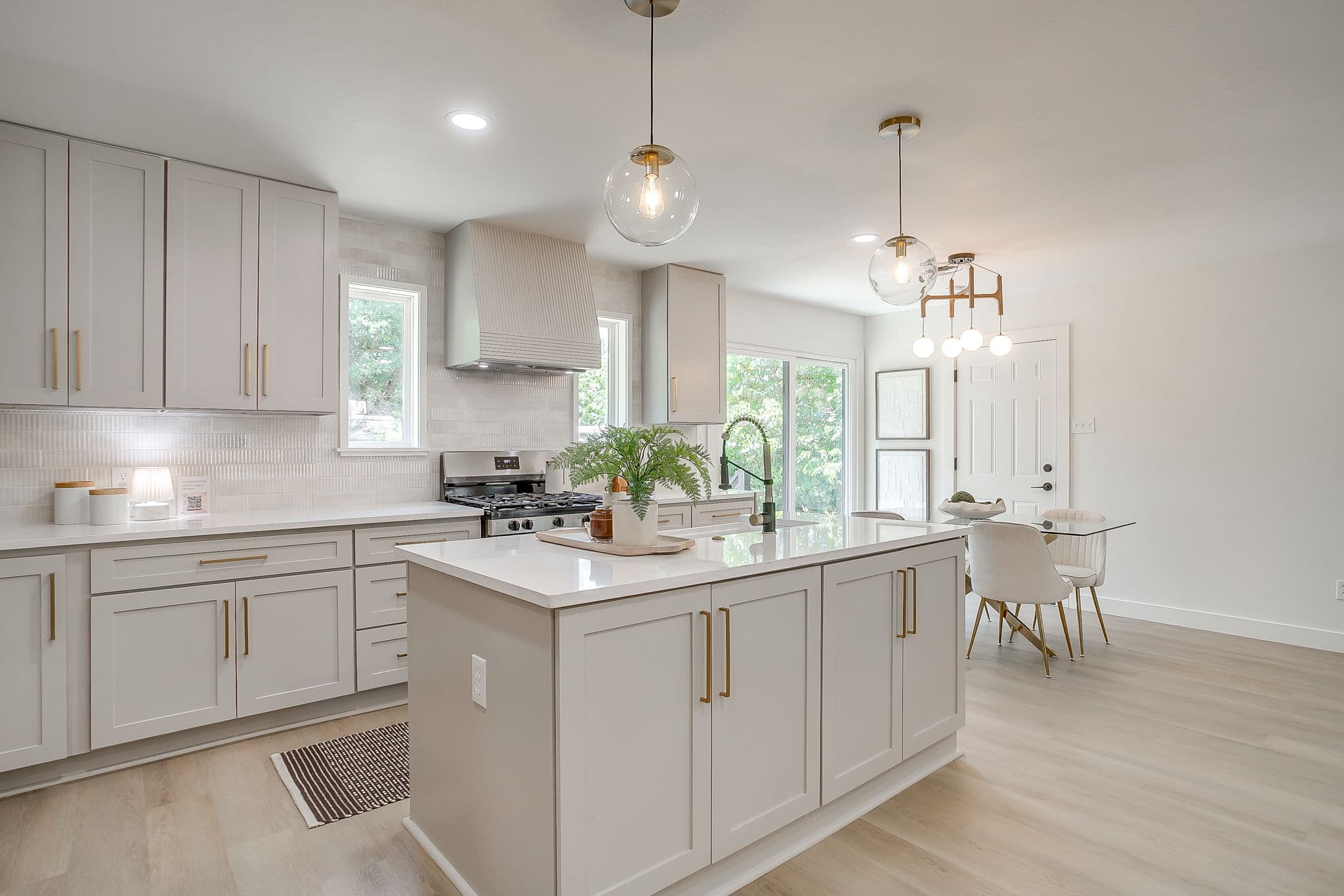 Modern kitchen with light gray cabinets, gold hardware, a white island, and globe pendant lighting.