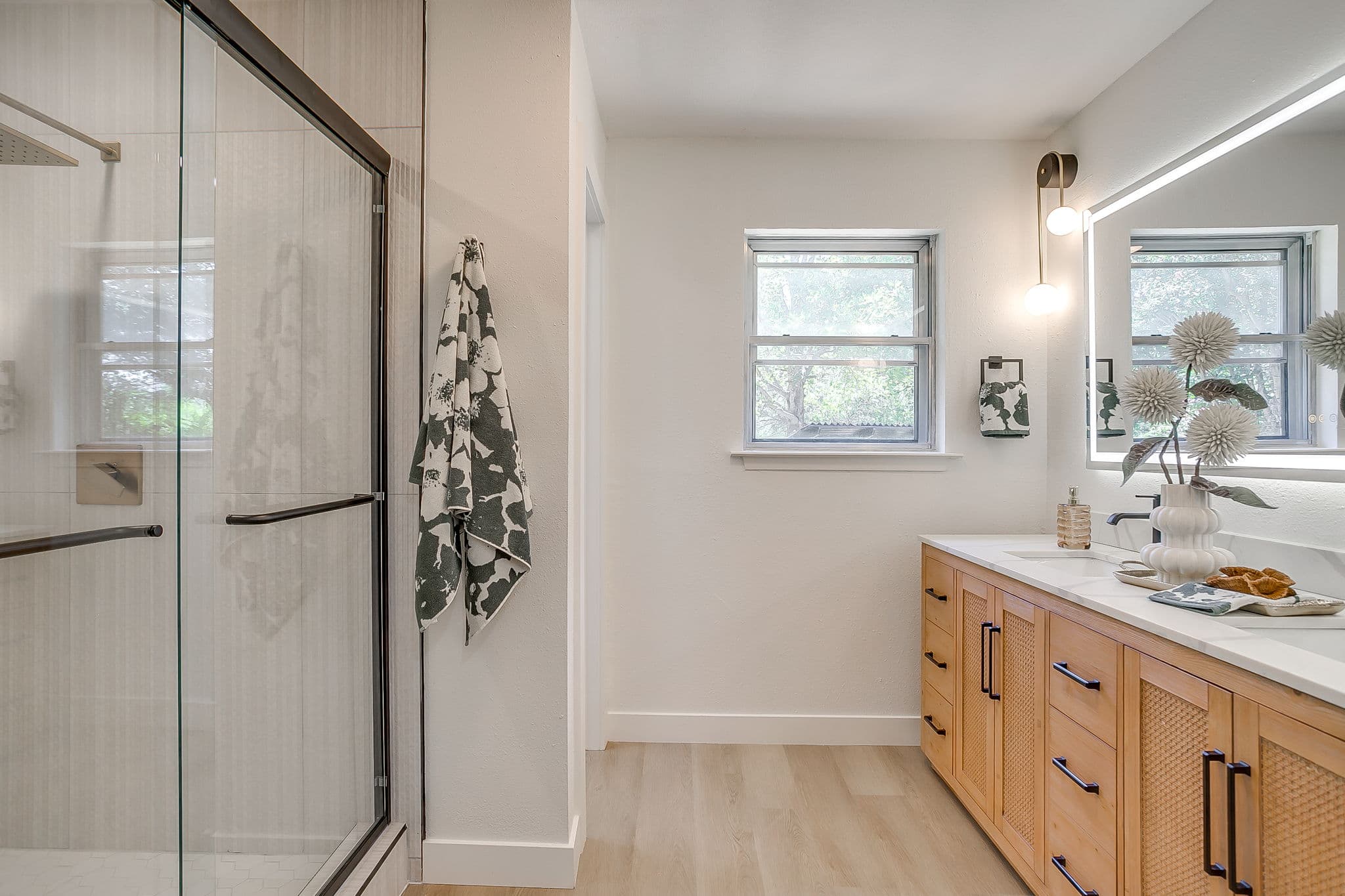 Modern bathroom with a glass shower, light wood vanity, and window providing natural light.