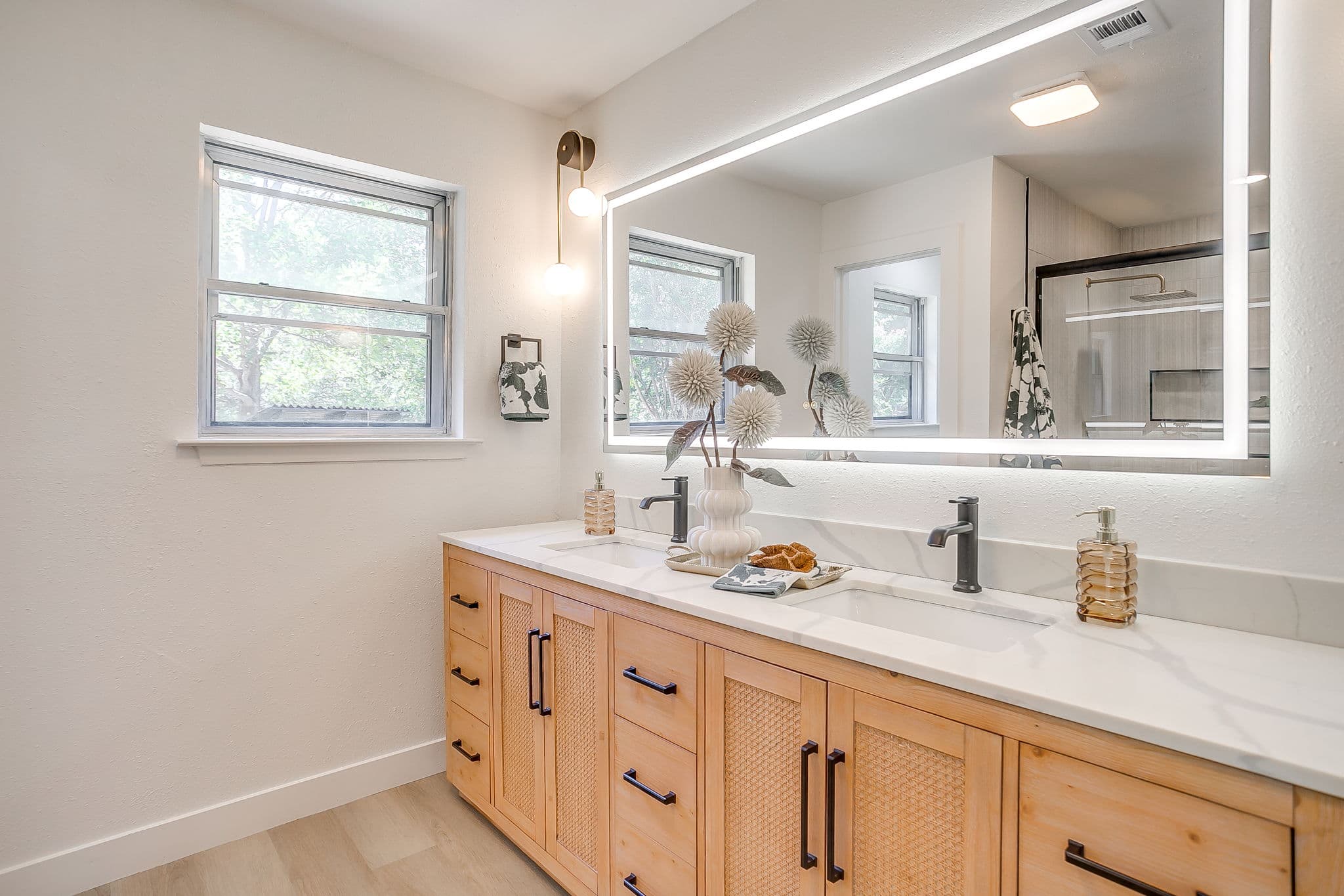 Modern bathroom with light wood double vanity, white marble countertop, and a large backlit mirror.