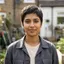Smiling person with short dark hair wearing a dark jacket in a residential garden.