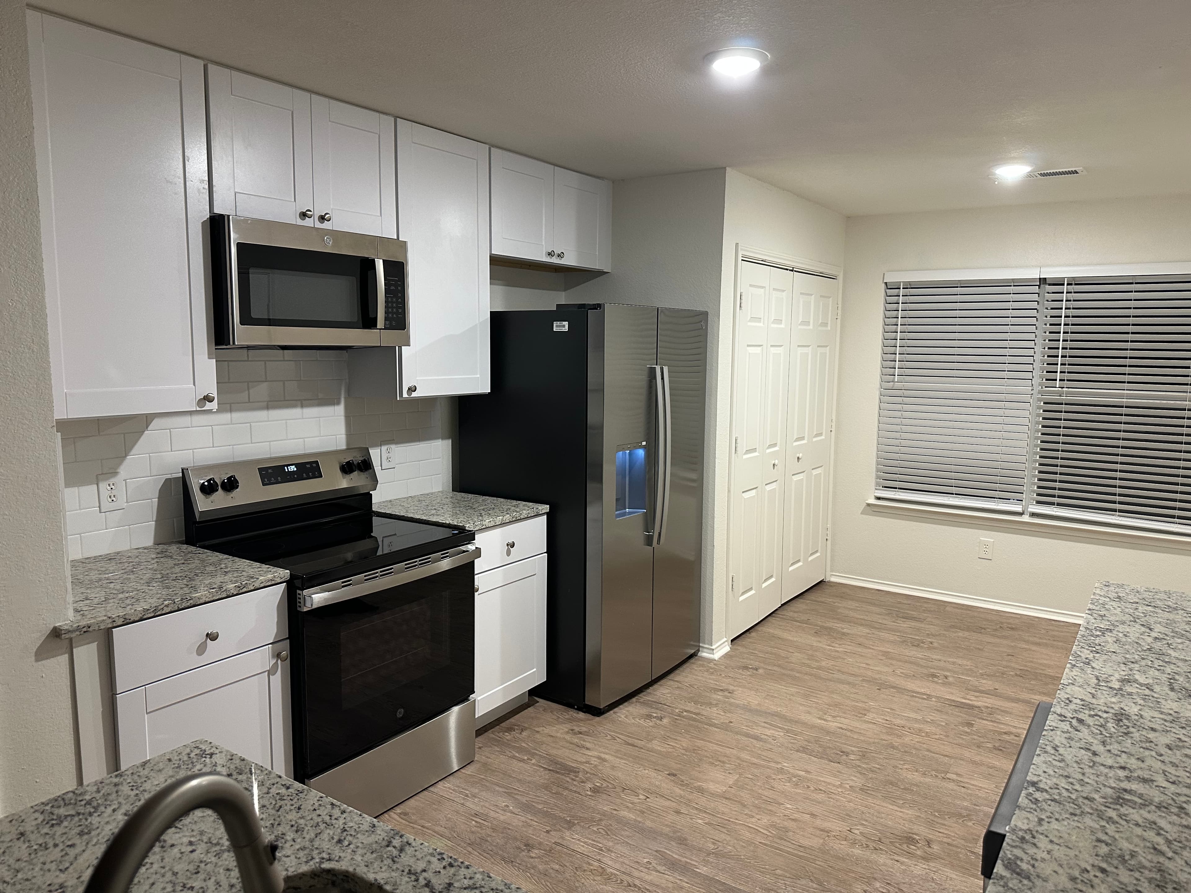 Modern kitchen with white cabinets, stainless steel appliances, granite countertops, and wood-look flooring.