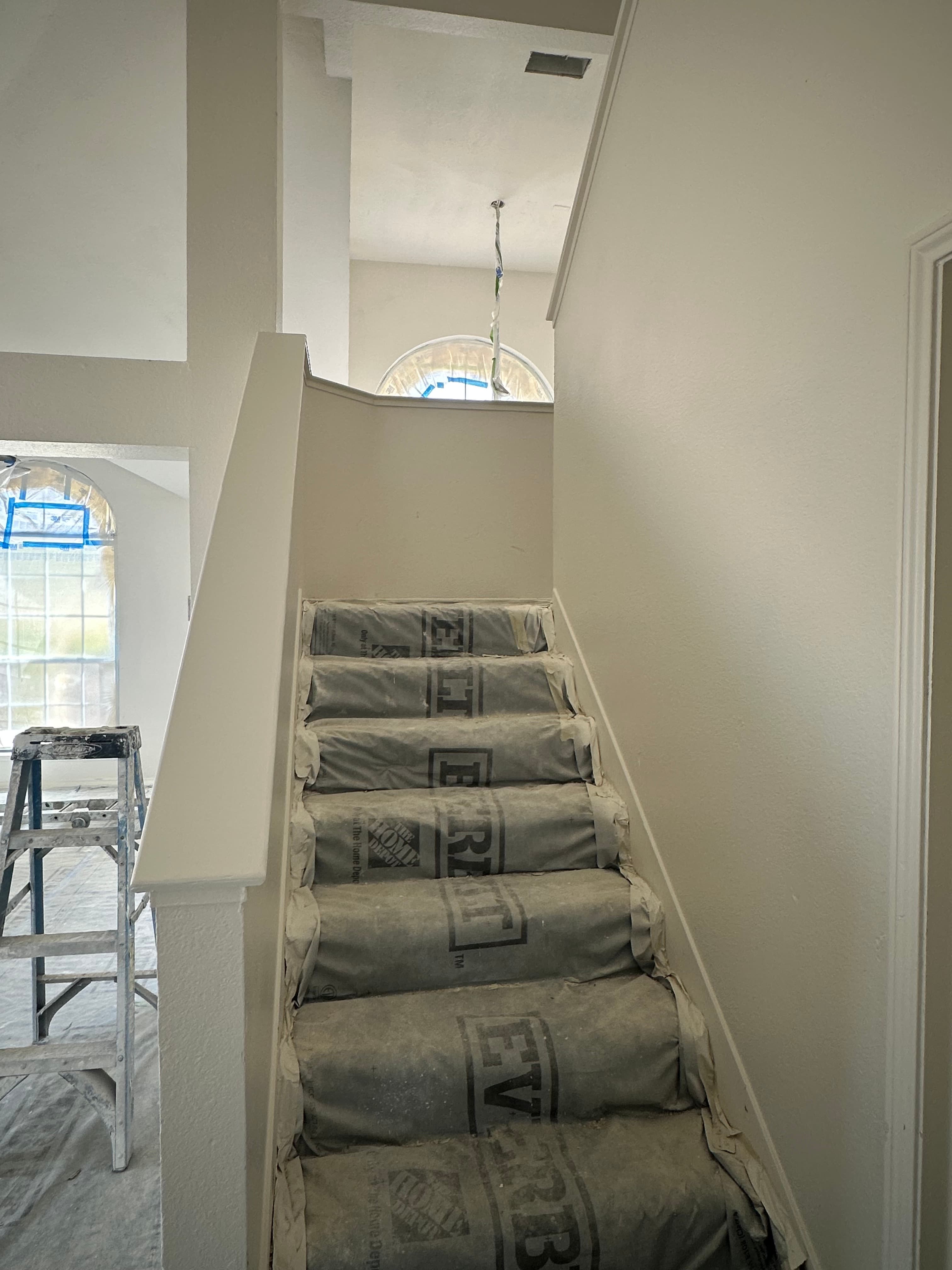 White staircase with steps covered in gray protective paper during an interior home renovation.