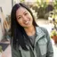 Smiling woman with long black hair tilting her head wearing a green utility jacket.