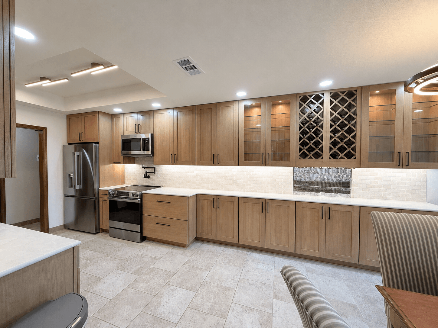 Modern kitchen with light wood cabinets, stainless steel appliances, white countertops, and wine storage.