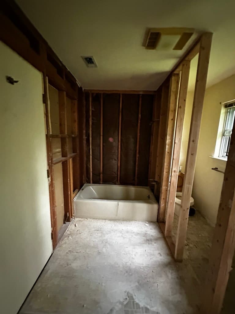 Bathroom renovation with exposed wooden studs, a white bathtub, and an unfinished concrete floor.