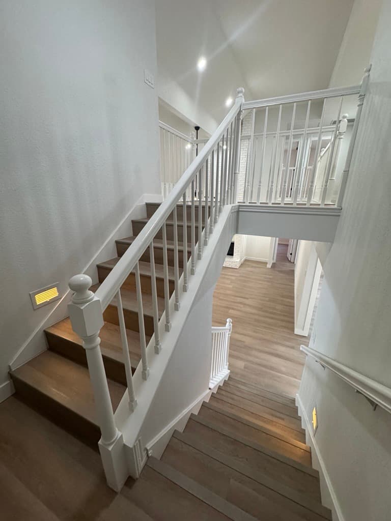 Modern wooden staircase with white railings and spindles in a bright, minimalist home interior.