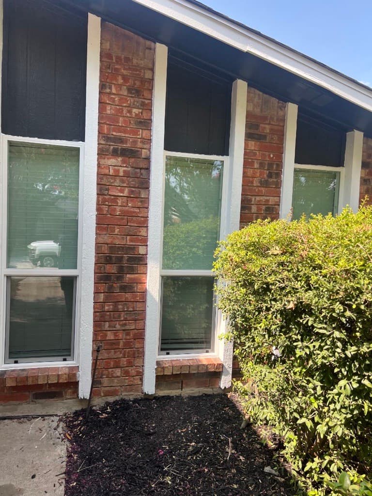 Red brick house exterior with tall white-trimmed windows, black siding panels, and a green bush.