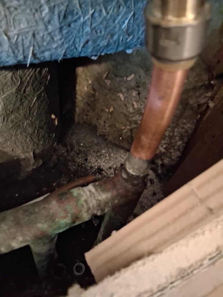 Corroded copper pipes with green oxidation and a push-fit connector surrounded by insulation.