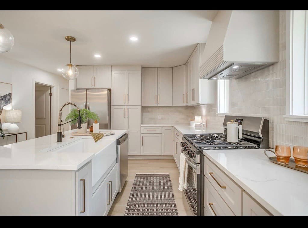 Modern kitchen featuring light gray cabinets, white countertops, a farmhouse sink, and gold hardware.