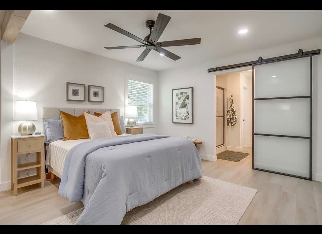 Modern bedroom with blue bedding, wooden nightstands, and a sliding frosted glass barn door.